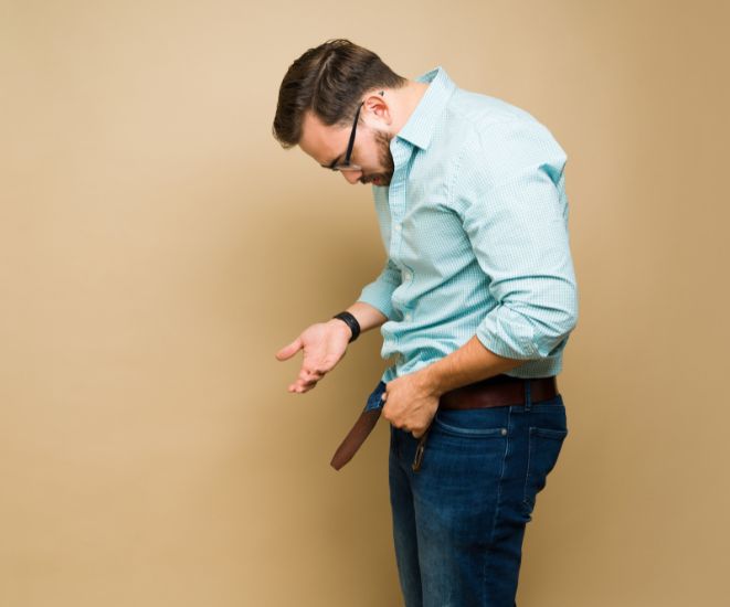 A man taking his belt off, looking down towards his hips.