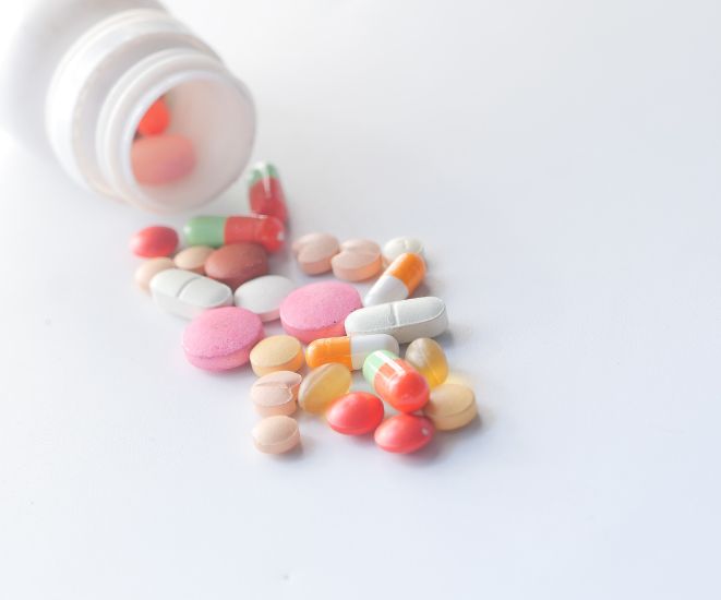 A white bottle with different colored pills spilling out of it.