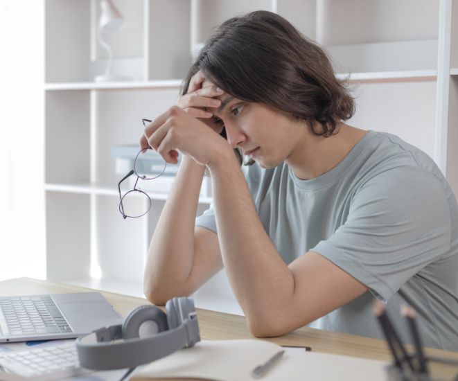 A woman sitting at a desk with a hand on her forehead. She looks stressed.