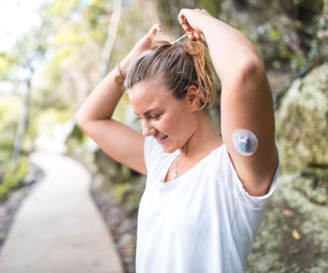 A woman in a white shirt with an insulin patch on her arm.