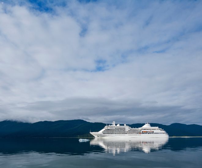 A cruise ship on the water, with clouds in the sky and land in the background.