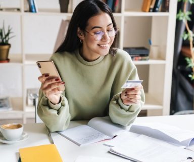 A woman holding a cell phone in one hand, and a credit card in the other.