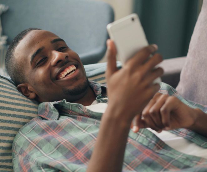 A man laying on a couch, looking at a cell phone.