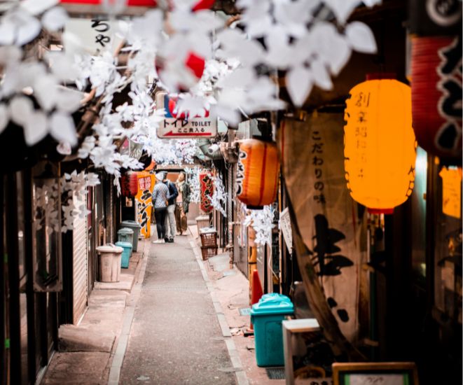 A small street in Japan, with cherry blossoms, store fronts and orange lanterns