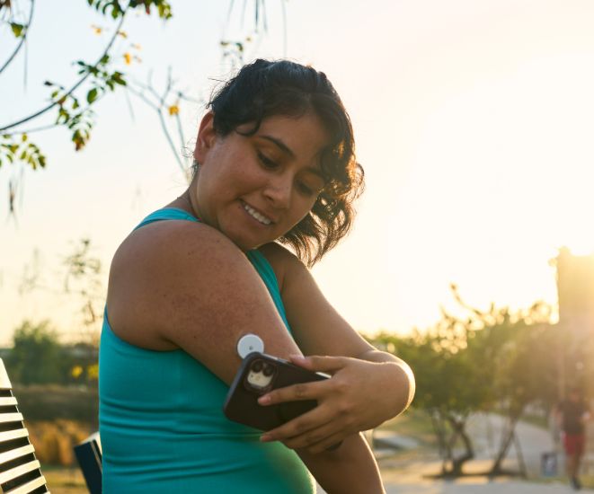 A diabetic woman sitting on a bench outside, checking her insulin levels
